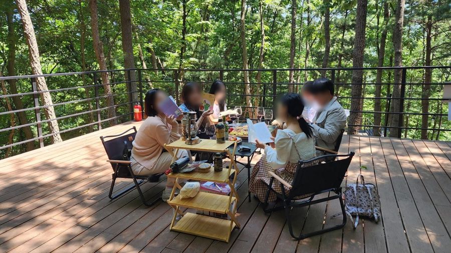 숲속 데크에 둘러앉아 책을 읽고 이야기하는 사람들